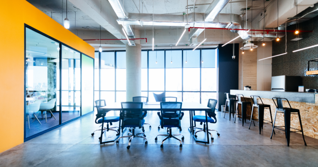 Workplace showing meeting room to the left, large meeting table in the centre and kitchen to the right.